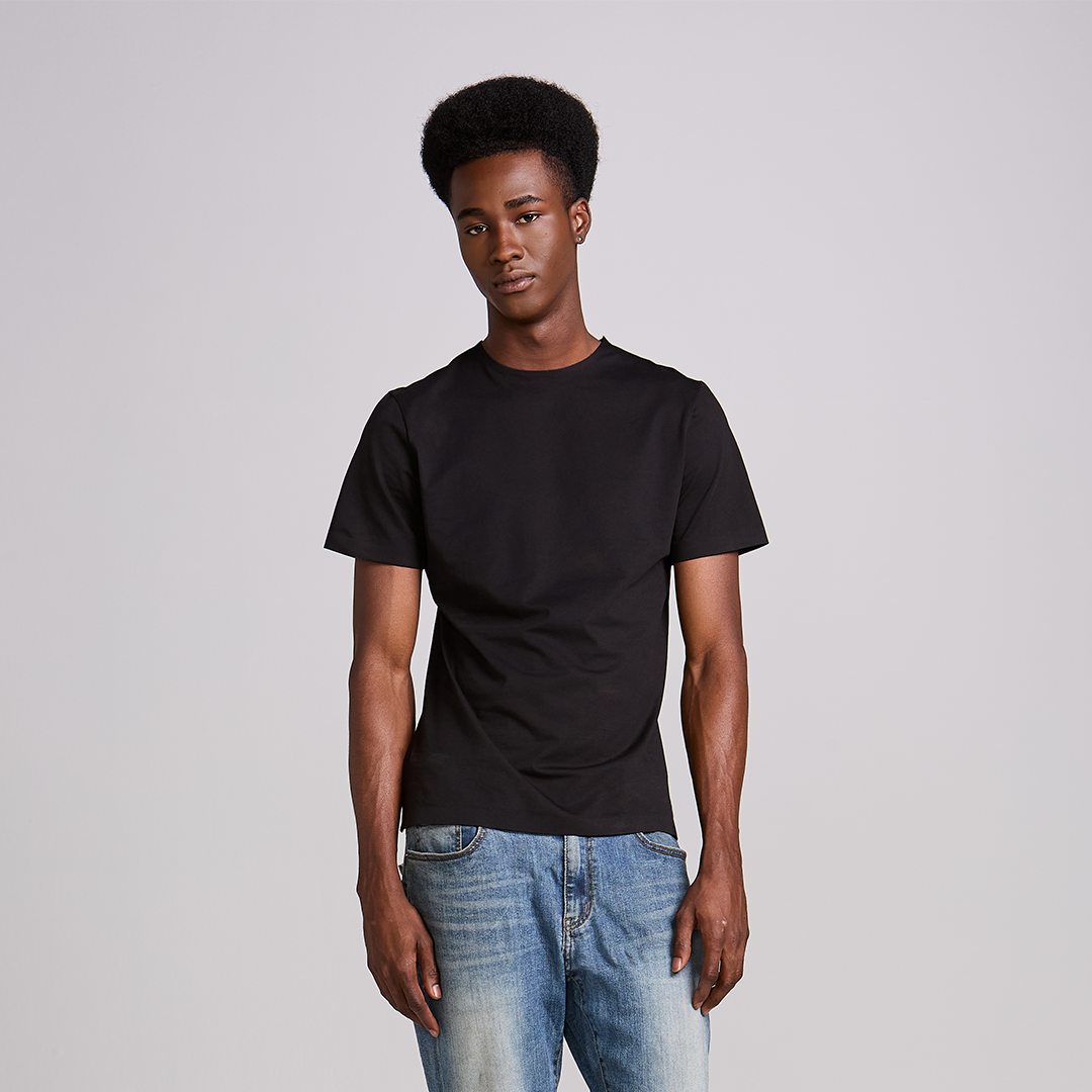 Homem de camiseta preta lisa e calça jeans em fundo neutro, look masculino básico e bem ajustado