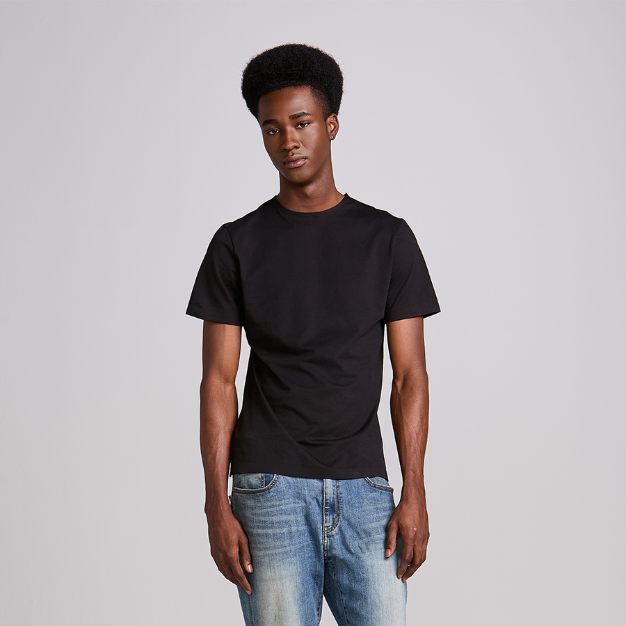Homem de camiseta preta lisa e calça jeans em fundo neutro, look masculino básico e bem ajustado