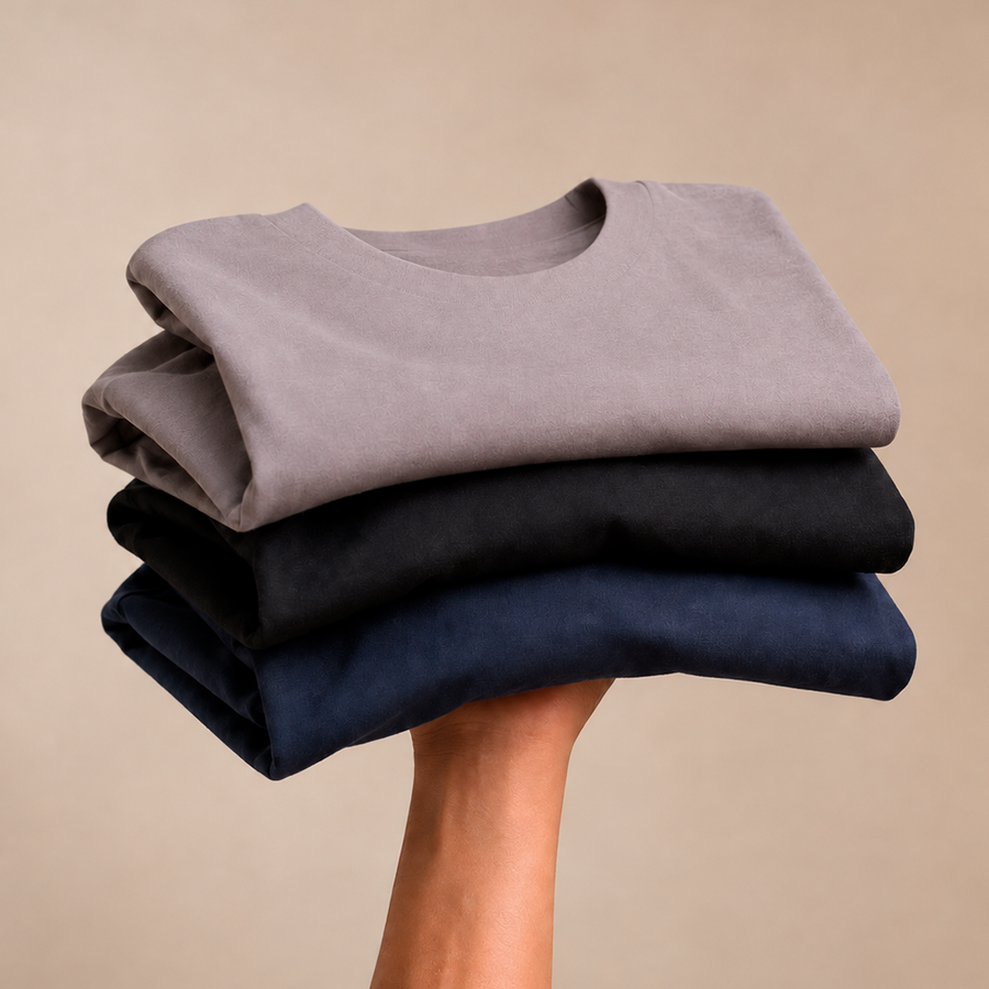 Três camisetas masculinas de algodão premium dobradas nas cores preto, azul marinho e cinza mescla